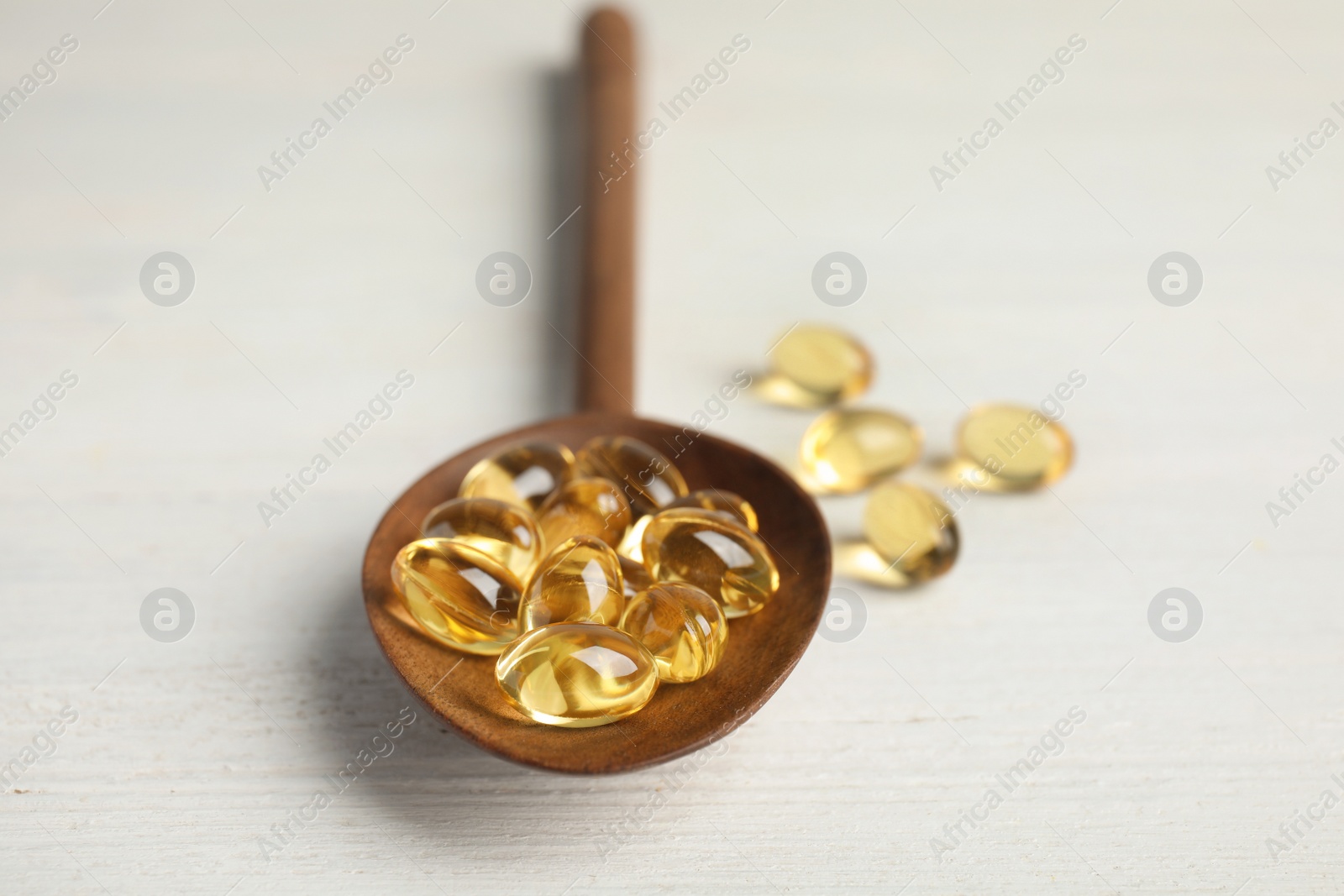 Photo of Spoon with cod liver oil pills on wooden background
