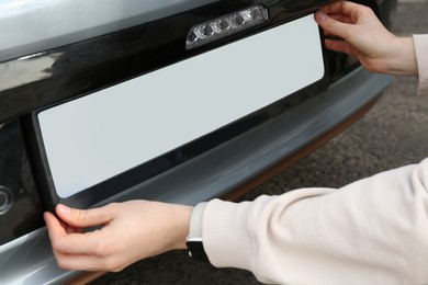 Photo of Woman installing vehicle registration plate outdoors, closeup