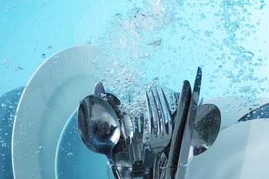 Washing silver cutlery and plates in water on light blue background