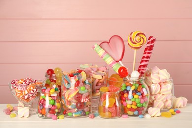 Photo of Jars with different delicious candies on white wooden table against pink background