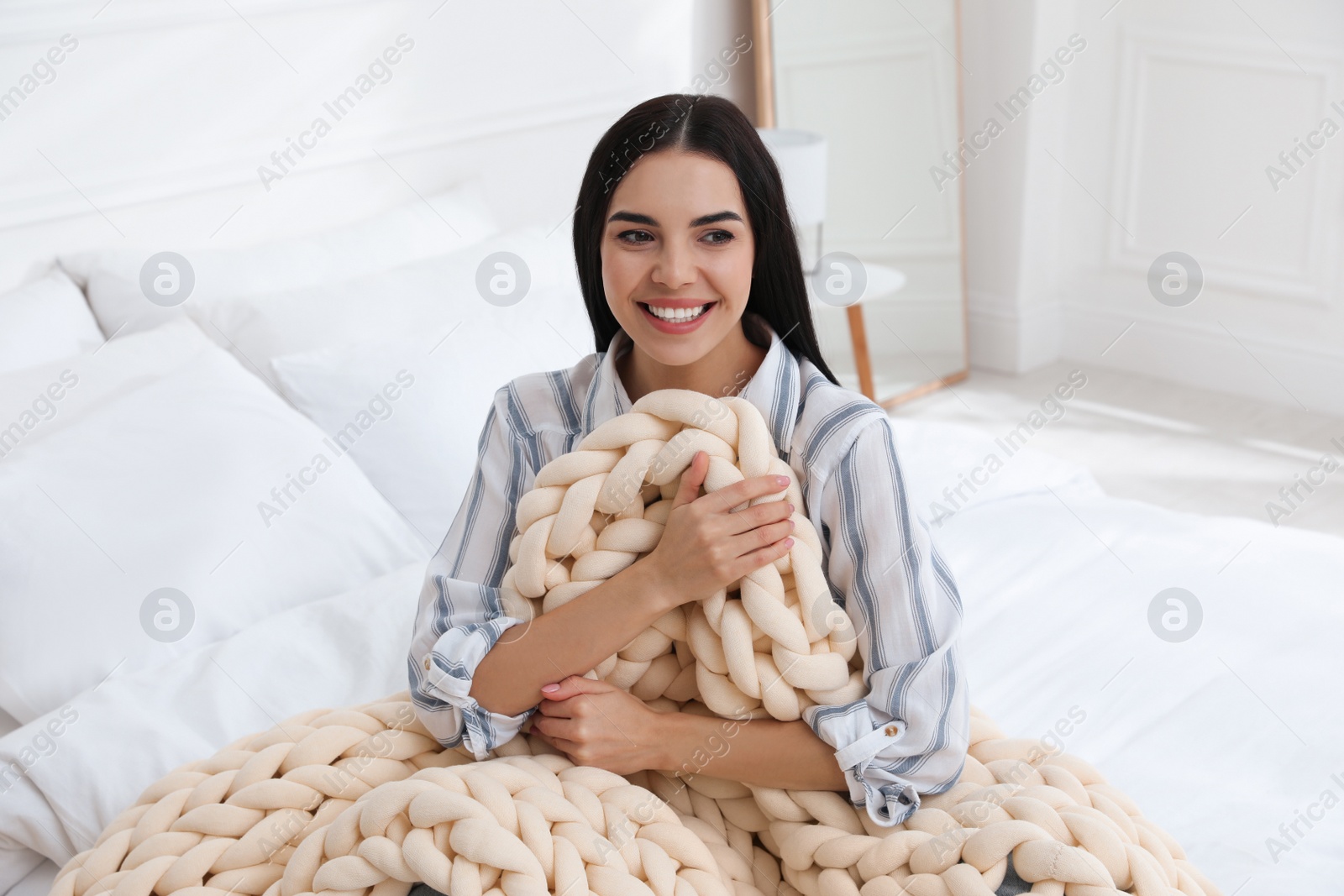 Photo of Young woman with chunky knit blanket on bed at home
