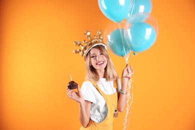Photo of Young woman with birthday muffin and air balloons on color background