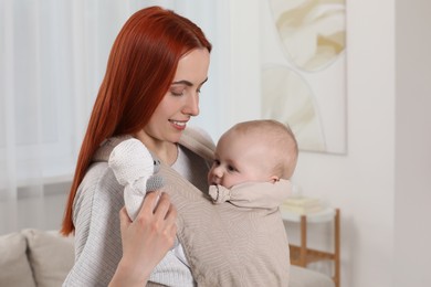 Mother holding her child in sling (baby carrier) at home