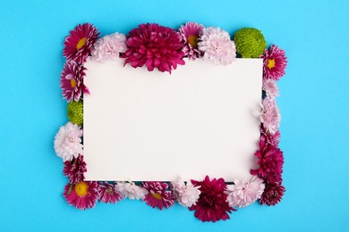 Beautiful chrysanthemum flowers and blank card on light blue background, flat lay. Space for text