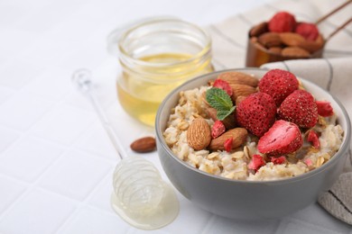 Photo of Delicious oatmeal with freeze dried strawberries, almonds and mint on white tiled table, closeup. Space for text