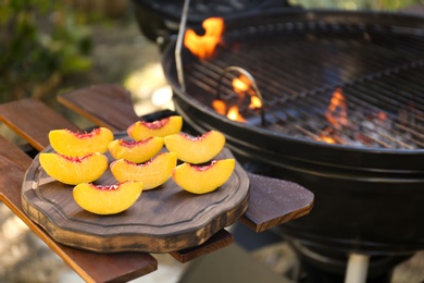 Photo of Slices of fresh peaches on wooden table near grill outdoors