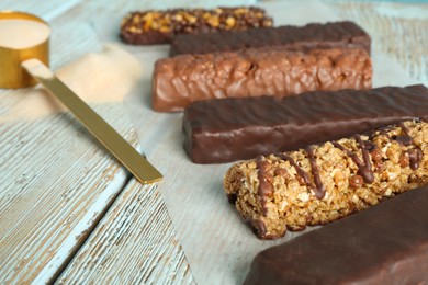 Different tasty bars and scoop of protein powder on wooden table, closeup