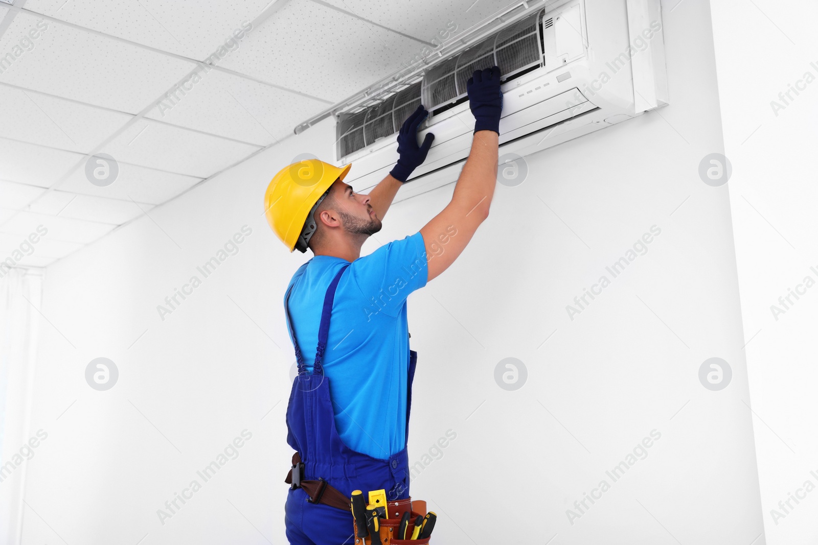 Photo of Professional technician maintaining modern air conditioner indoors