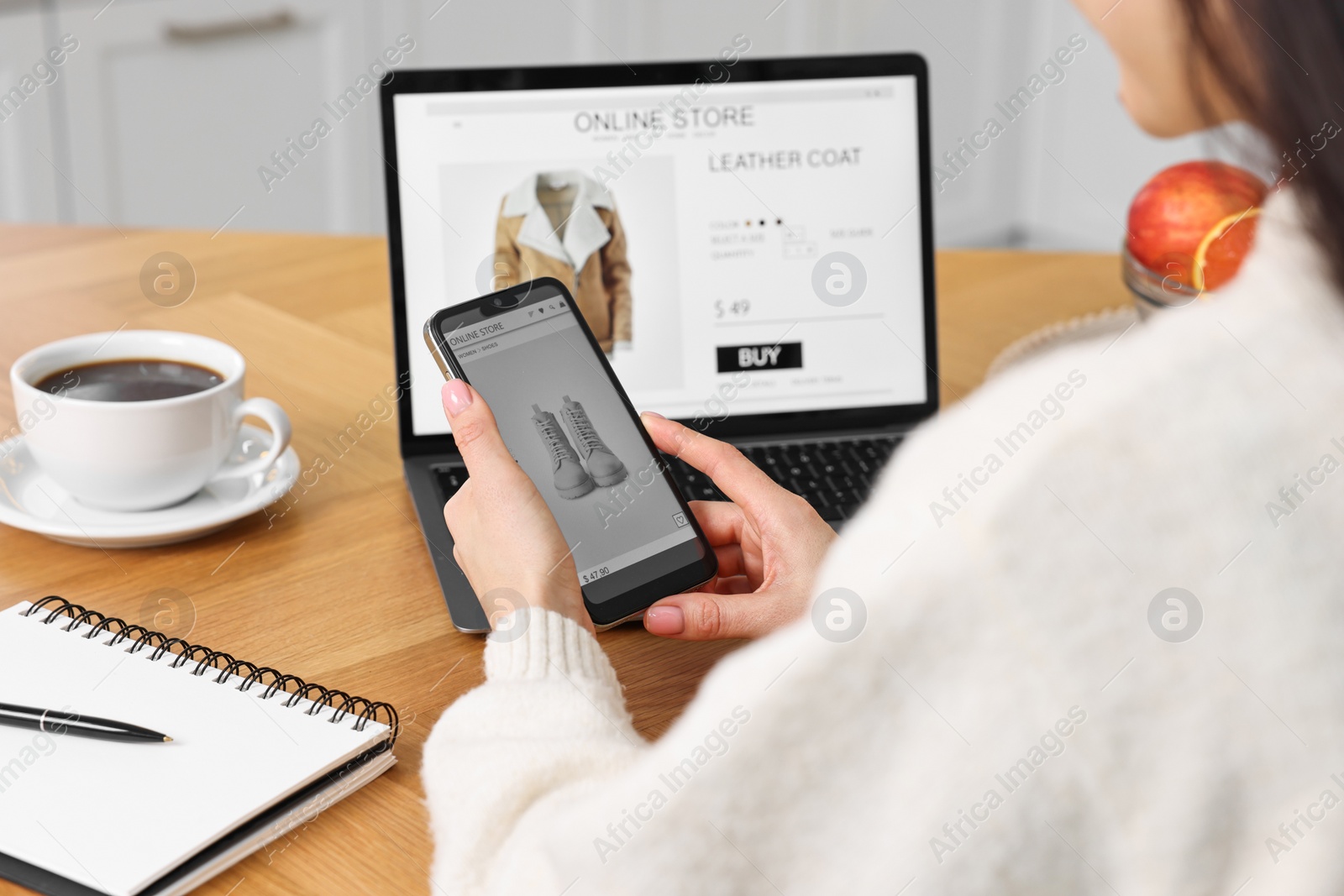 Photo of Woman with laptop and smartphone shopping online at wooden table in kitchen, closeup