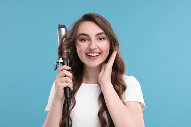 Photo of Beautiful young woman using curling hair iron on light blue background