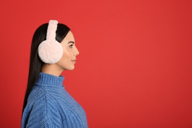 Beautiful young woman wearing earmuffs on red background. Space for text