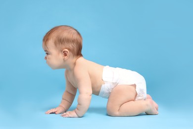 Photo of Cute little baby in diaper crawling on light blue background