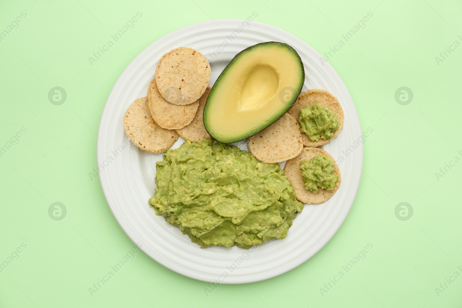 Photo of Delicious guacamole, avocado and chips on light green background, top view
