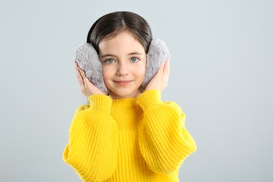 Photo of Cute girl wearing stylish earmuffs on grey background