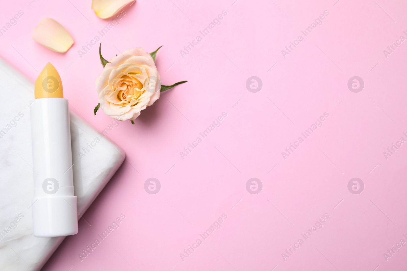 Photo of Hygienic lipstick, marble board and rose flower on pink background, flat lay. Space for text