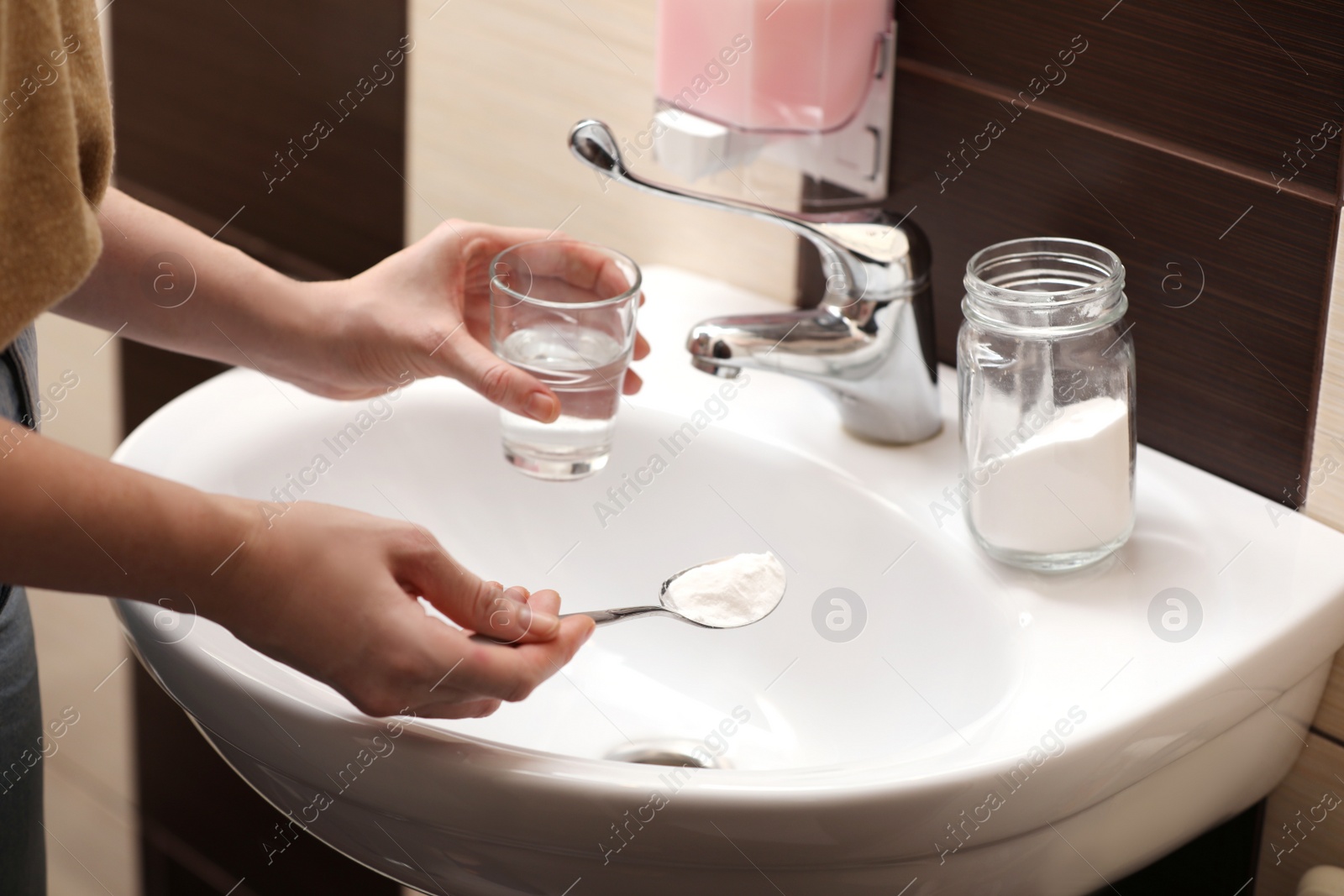 Photo of Woman using baking soda to unclog sink drain in bathroom, closeup