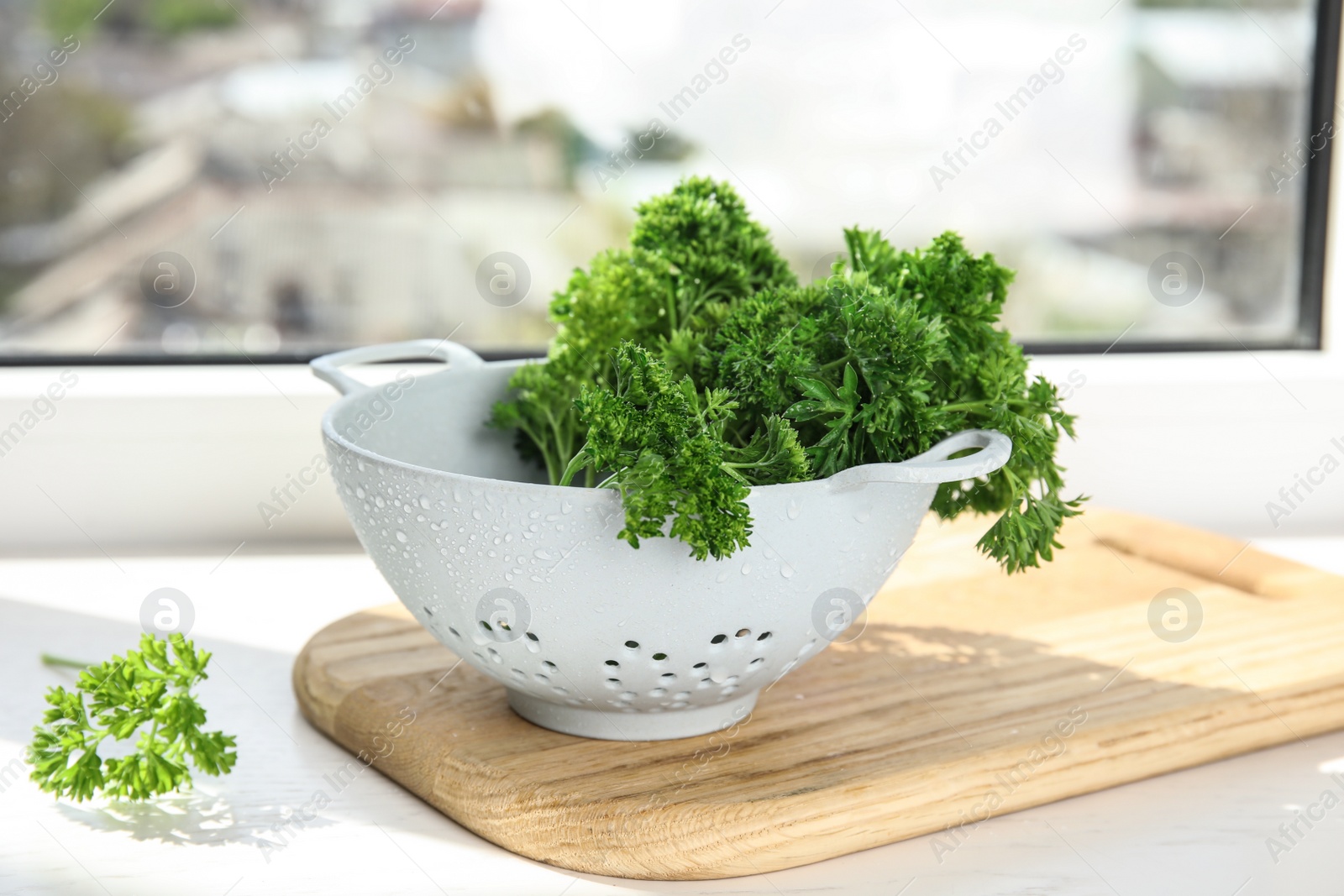 Photo of Colander with fresh green parsley on window sill indoors