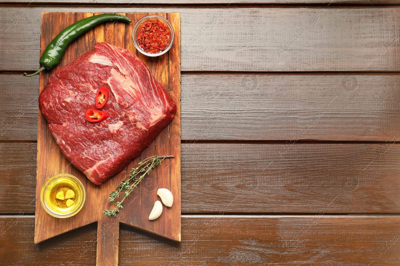 Photo of Fresh raw beef cut, spices and oil on wooden table, top view. Space for text