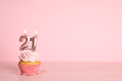 Photo of Coming of age party - 21th birthday. Delicious cupcake with number shaped candles on pink background, space for text