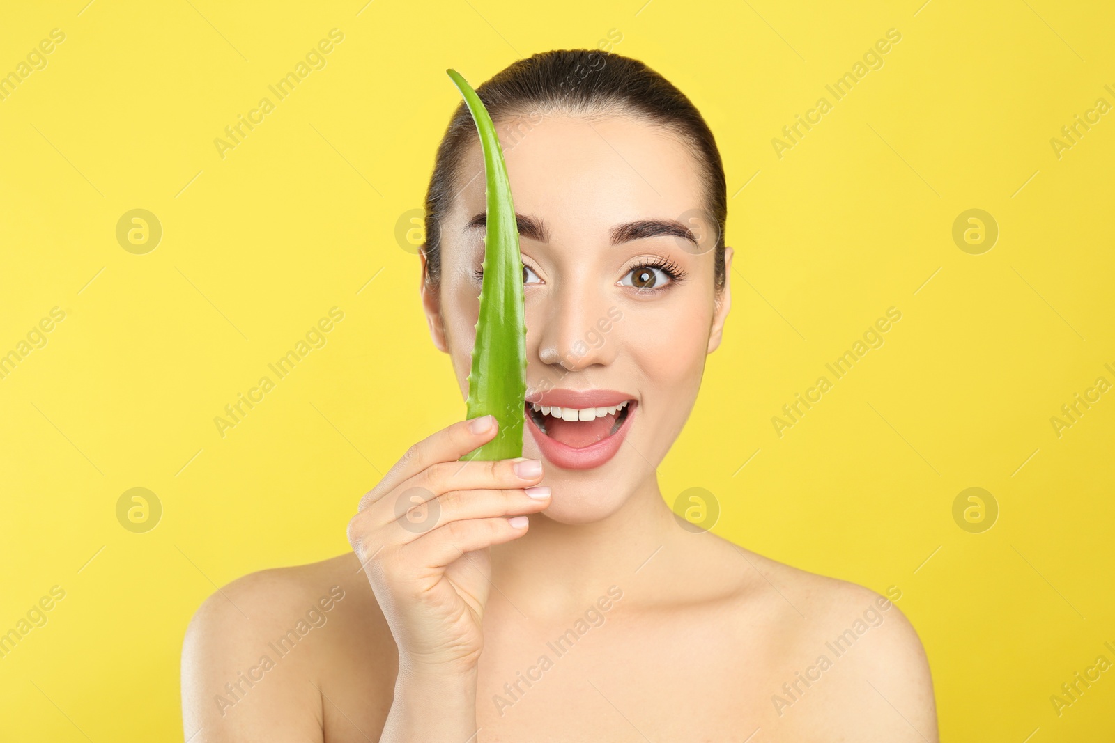 Photo of Emotional young woman with aloe vera leaf on yellow background