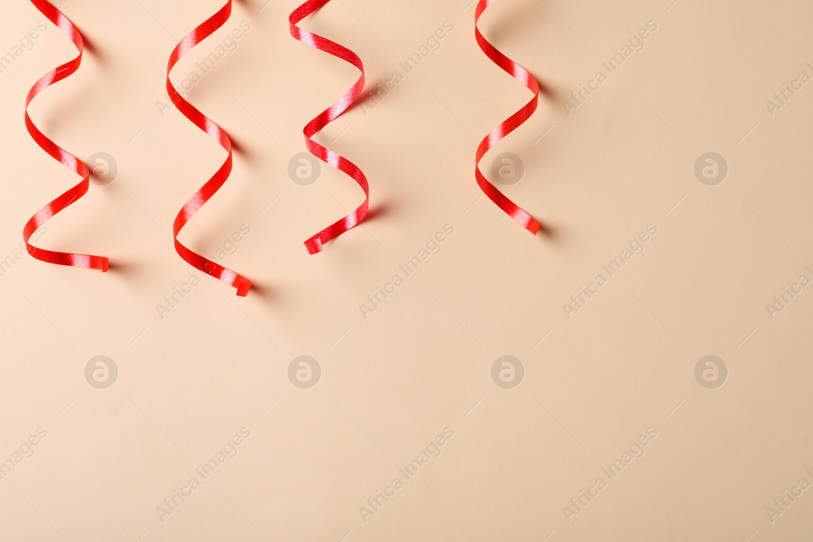 Photo of Shiny red serpentine streamers on beige background, flat lay. Space for text