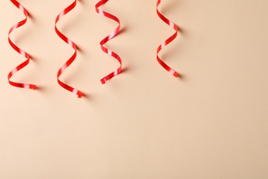 Photo of Shiny red serpentine streamers on beige background, flat lay. Space for text