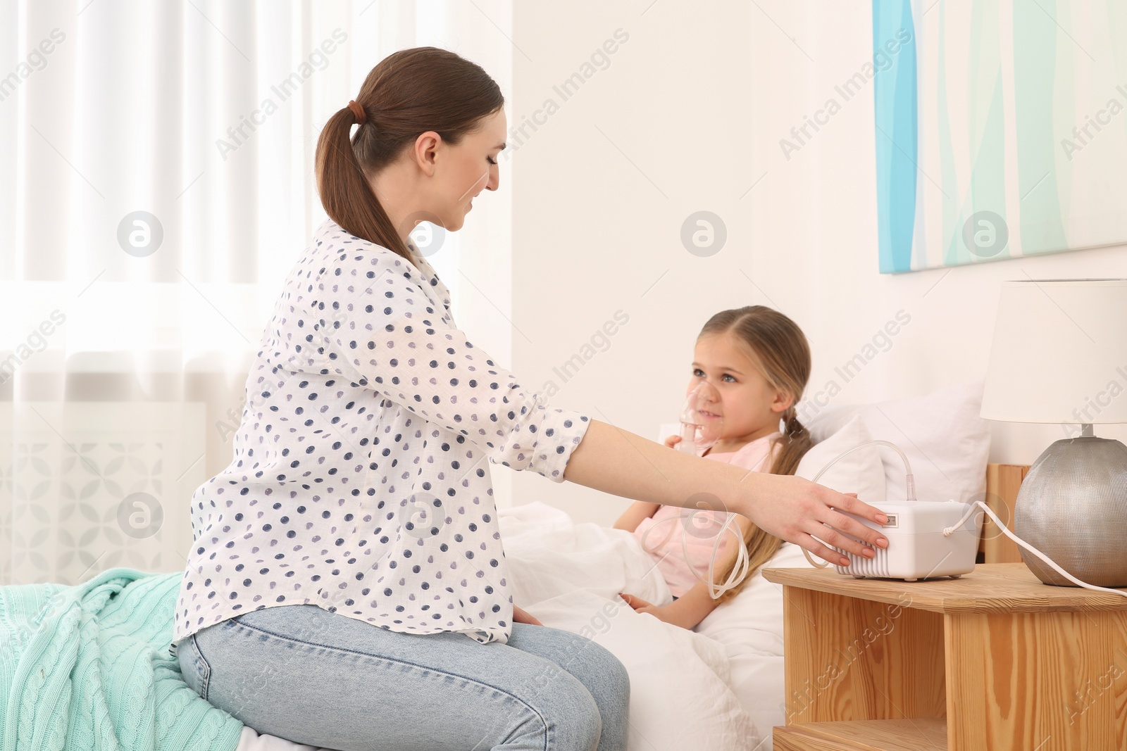 Photo of Mother helping her sick daughter with nebulizer inhalation in bedroom