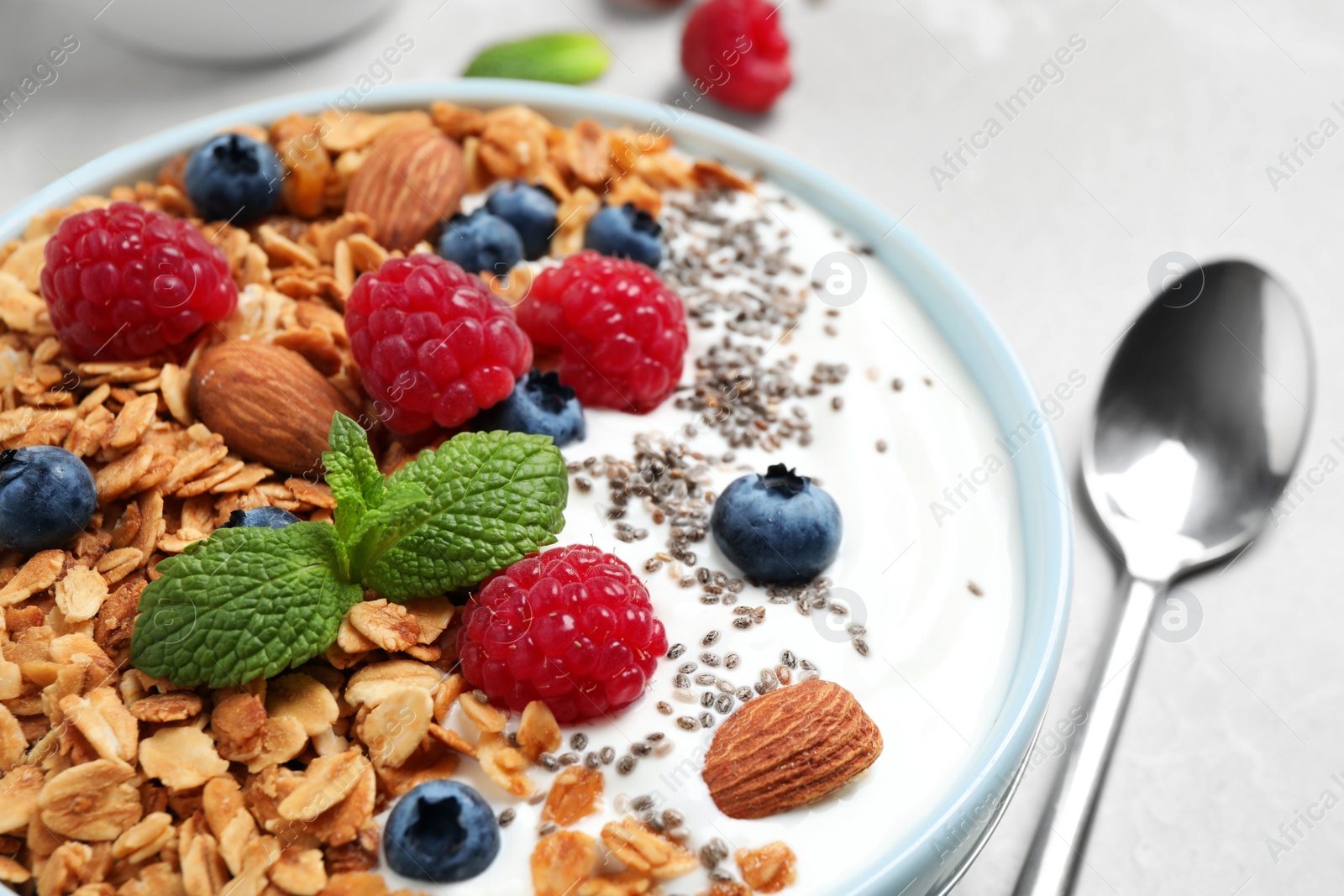 Photo of Tasty homemade granola with yogurt and berries on light grey table, closeup. Healthy breakfast