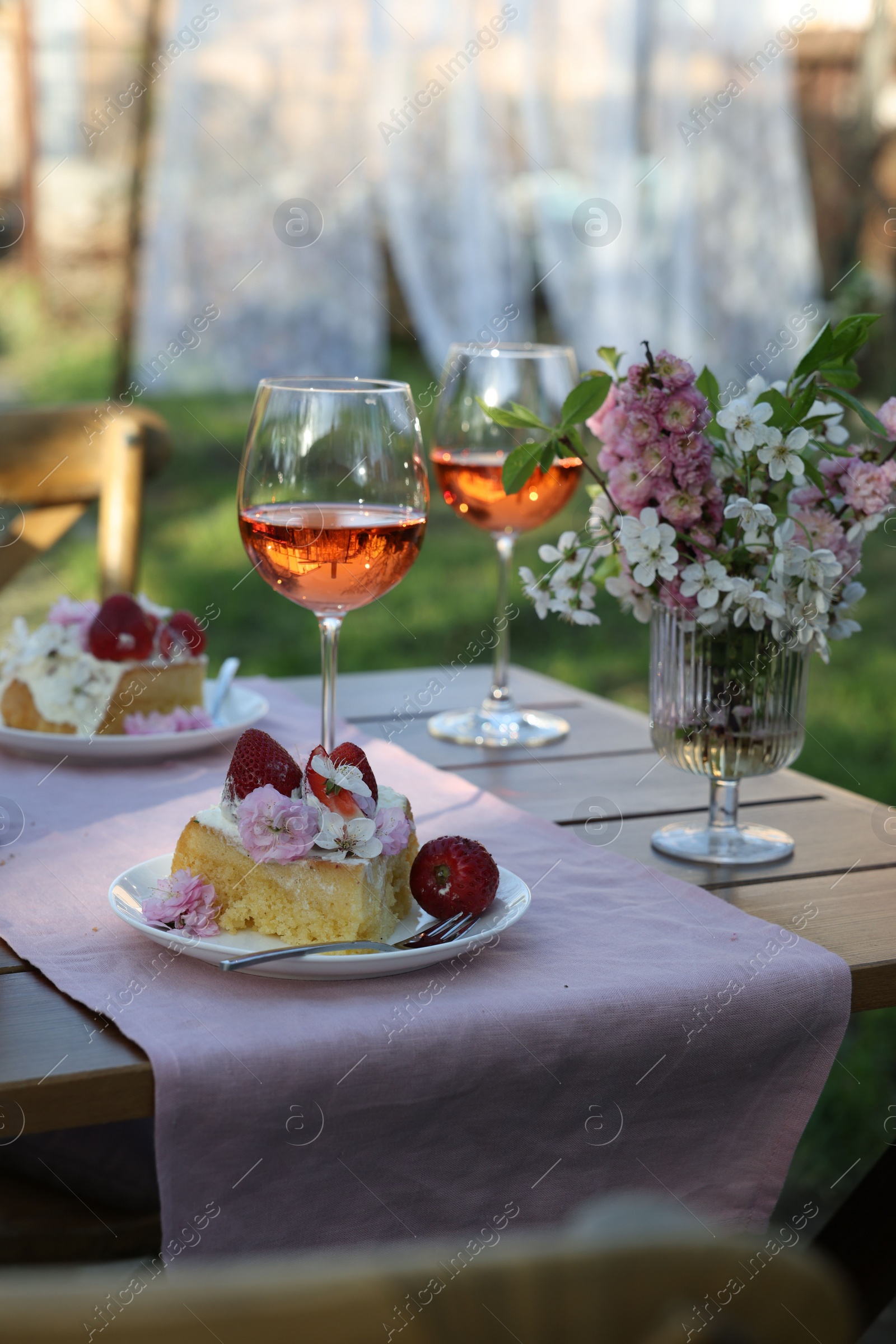 Photo of Vase with spring flowers, wine and cake on table served for romantic date in garden