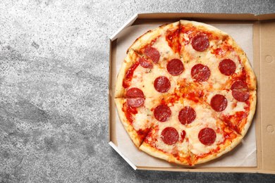 Photo of Hot delicious pepperoni pizza in cardboard box on grey table, top view. Space for text