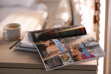 Photo of Open sports magazine, notebooks and coffee on cabinet indoors