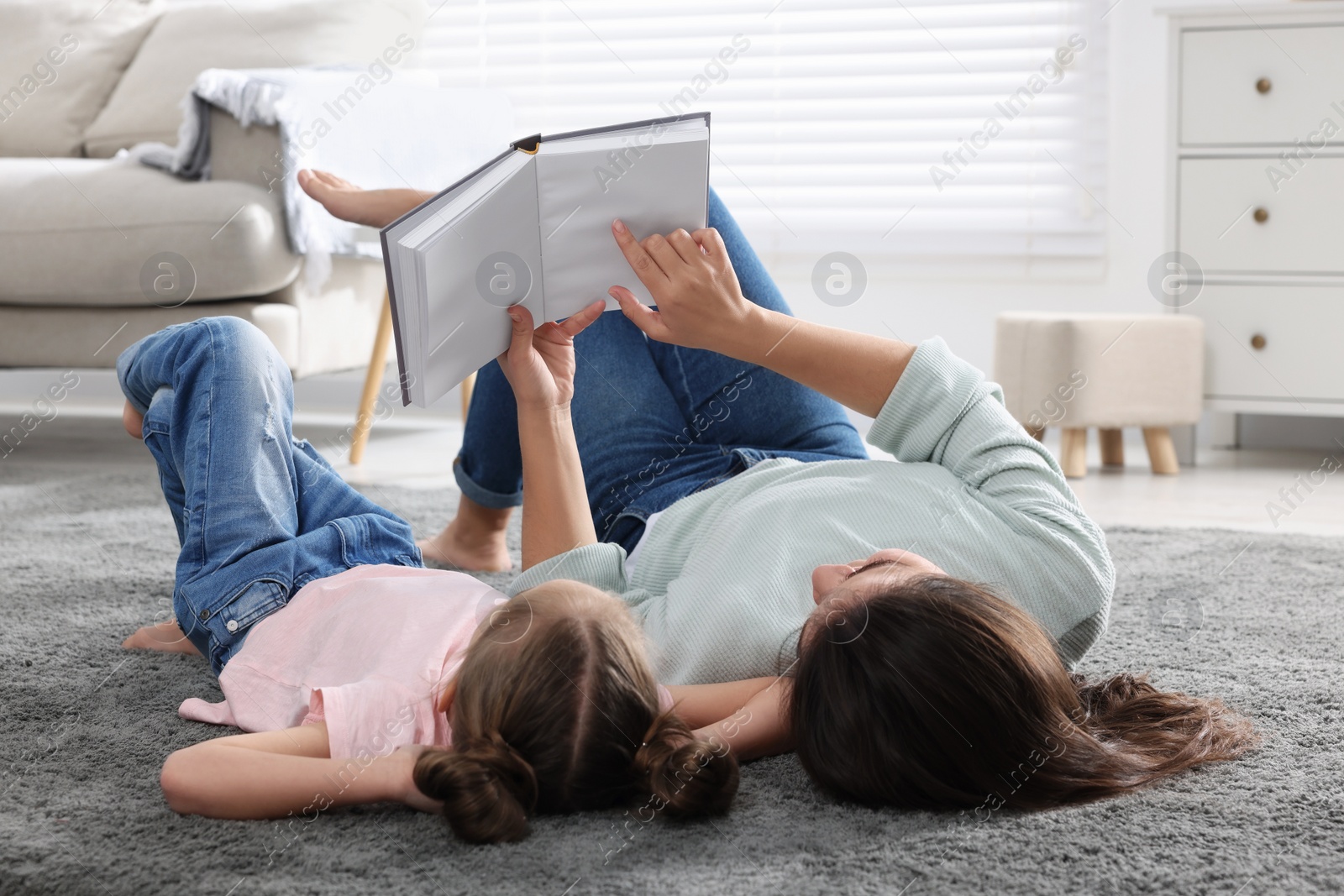 Photo of Young mother and her daughter reading book on floor at home