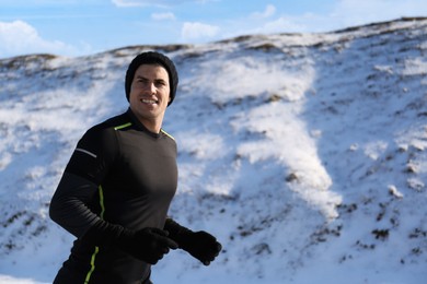 Photo of Happy man running past snowy hill in winter. Outdoors sports exercises