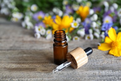 Photo of Bottle of essential oil and flowers on wooden table