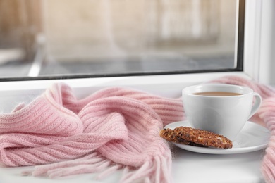 Cup of winter drink, cookies and knitted scarf on windowsill. Space for text