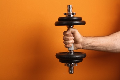 Photo of Male athlete holding metal dumbbell on color background. Space for text