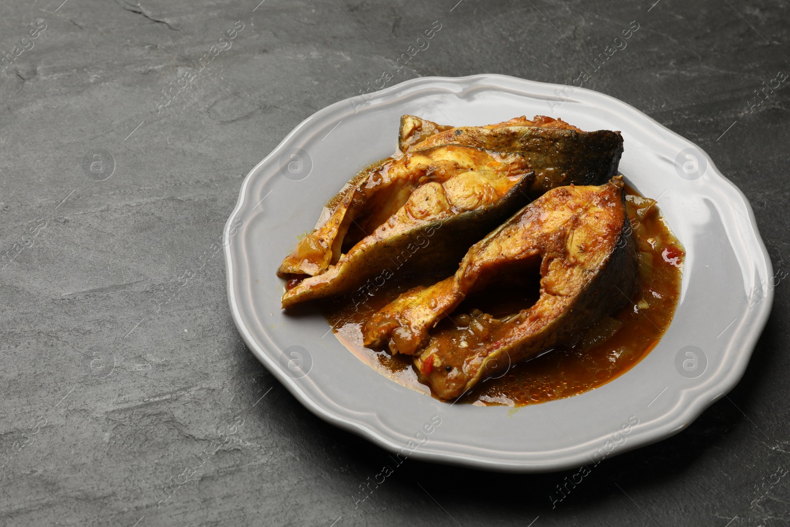 Photo of Tasty fish curry on grey textured table, closeup. Space for text. Indian cuisine