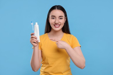 Photo of Happy young woman holding plastic toothbrush and tube of toothpaste on light blue background