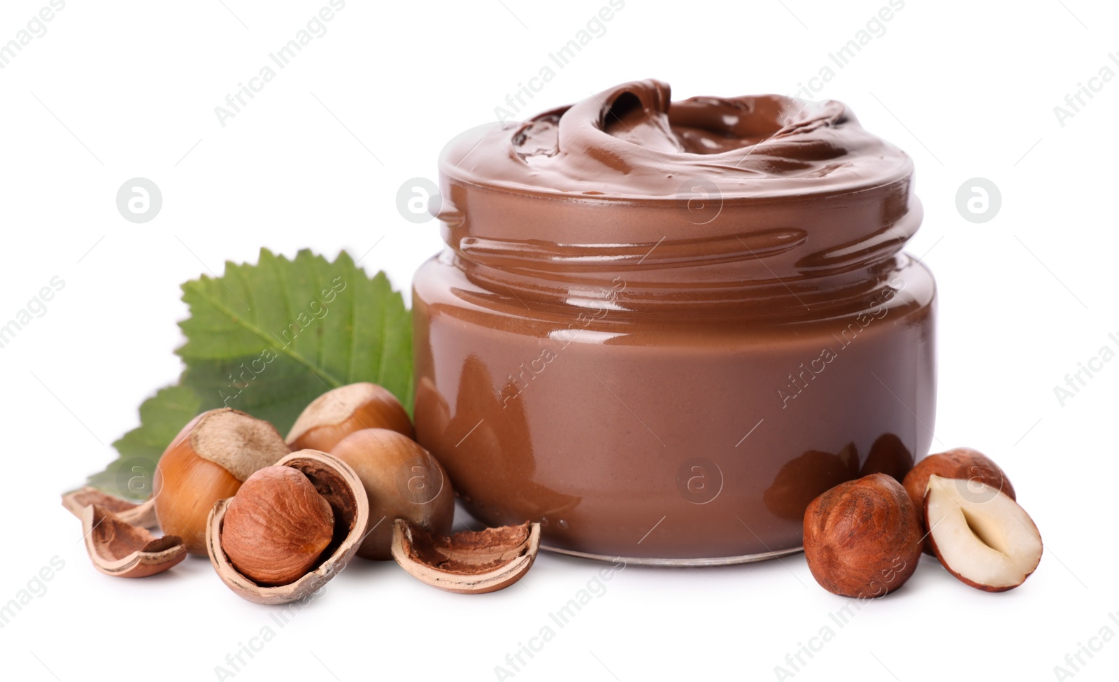 Photo of Glass jar with tasty chocolate spread, hazelnuts and green leaves on white background