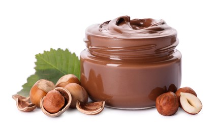 Glass jar with tasty chocolate spread, hazelnuts and green leaves on white background