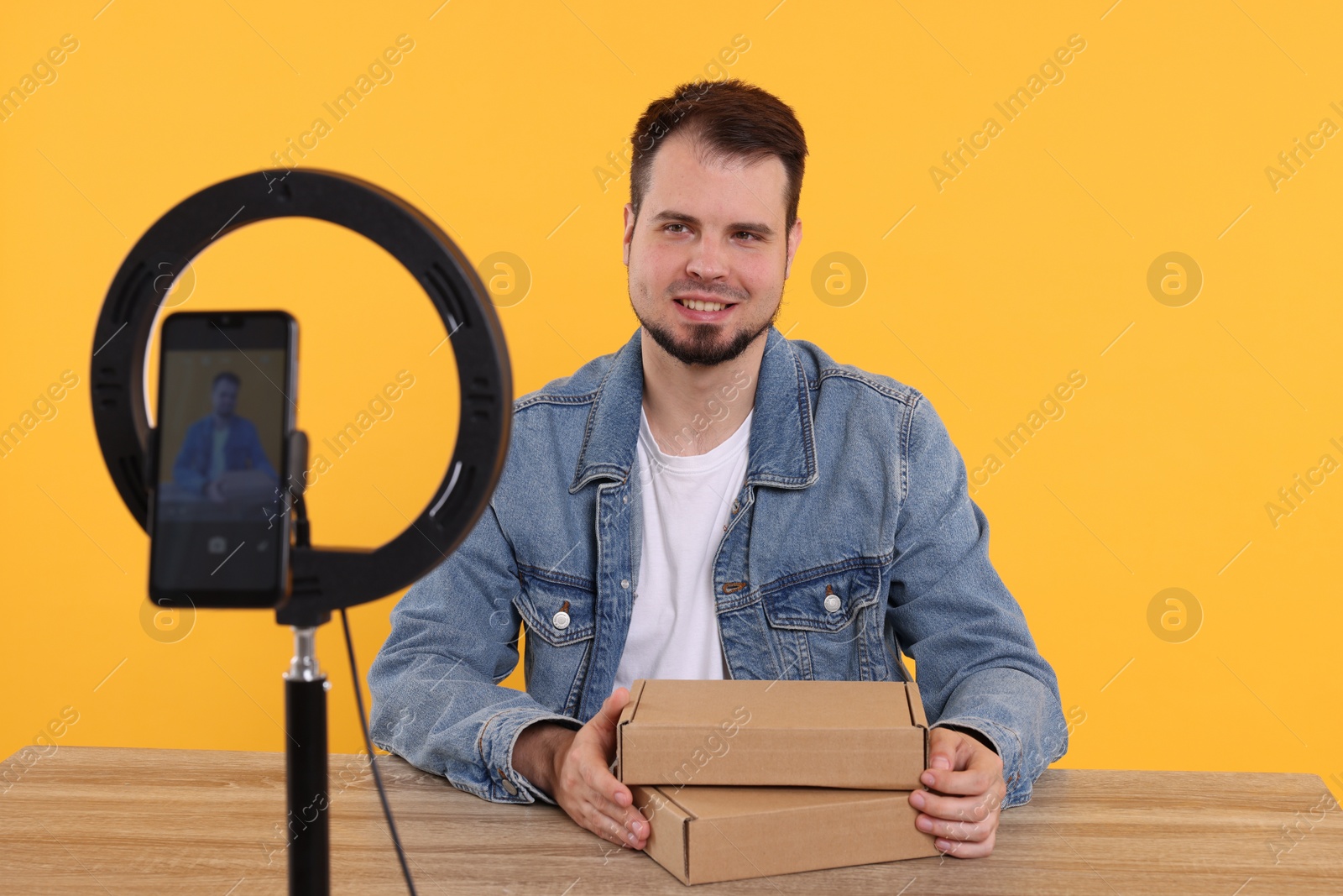 Photo of Smiling fashion blogger with parcels recording video at table against orange background