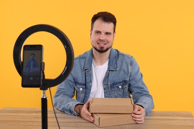 Smiling fashion blogger with parcels recording video at table against orange background