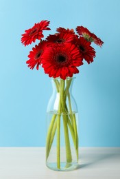 Photo of Bouquet of beautiful red gerbera flowers in glass vase on light blue background