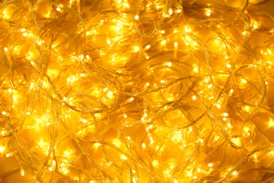 Glowing Christmas lights on yellow background, top view