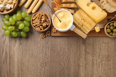 Photo of Flat lay composition with pot of tasty cheese fondue on wooden table, space for text