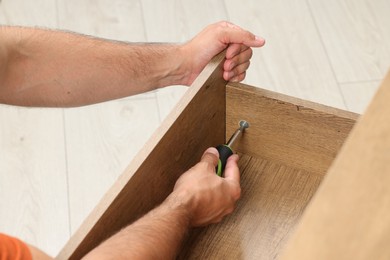 Photo of Man with screwdriver assembling drawer indoors, closeup