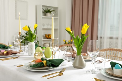 Photo of Festive Easter table setting with painted eggs, burning candles and yellow tulips indoors