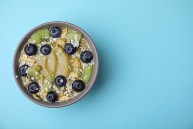 Bowl of delicious fruit smoothie with fresh blueberries, kiwi slices and coconut flakes on light blue background, top view. Space for text