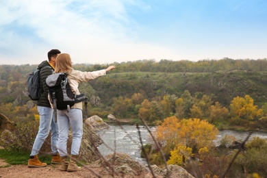 Photo of Couple of hikers with travel backpacks enjoying beautiful view near mountain river