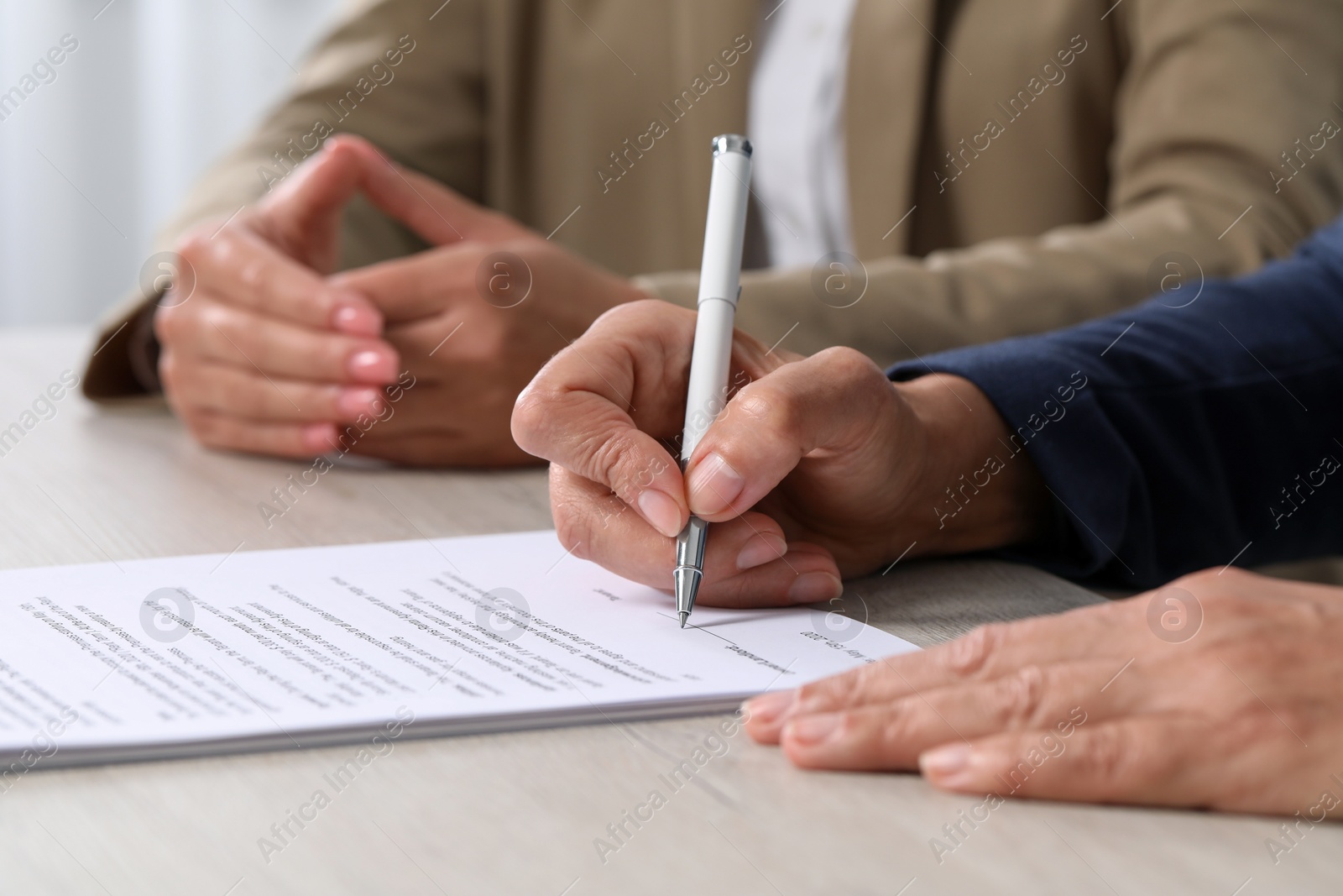 Photo of Signing document. Women at light wooden table indoors, closeup